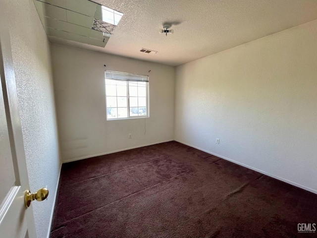 unfurnished room featuring visible vents, dark colored carpet, and a textured ceiling