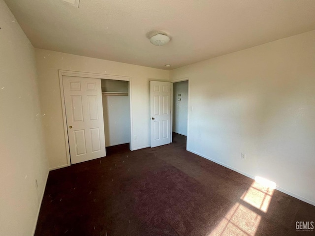 unfurnished bedroom with dark colored carpet, a closet, and baseboards