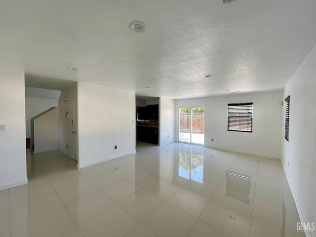 empty room featuring light tile patterned floors, baseboards, and a textured ceiling