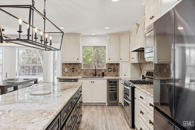 7544 Clifford Ct, Bakersfield, CA 93313 - kitchen featuring appliances with stainless steel finishes, beverage cooler, a sink, light wood-style floors, and light stone counters
