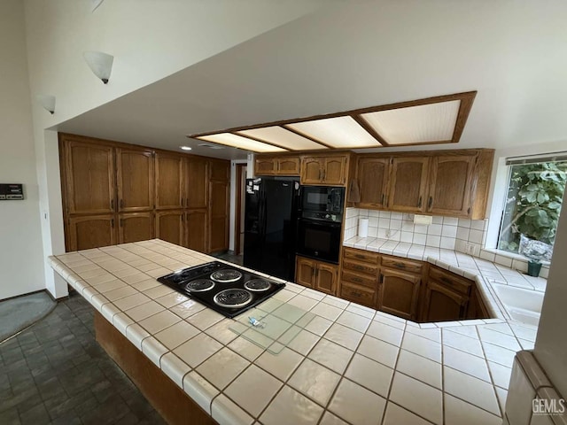 kitchen featuring brown cabinets, tile counters, a peninsula, tasteful backsplash, and black appliances