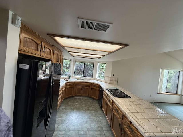 kitchen with tile countertops, a peninsula, a healthy amount of sunlight, visible vents, and black appliances