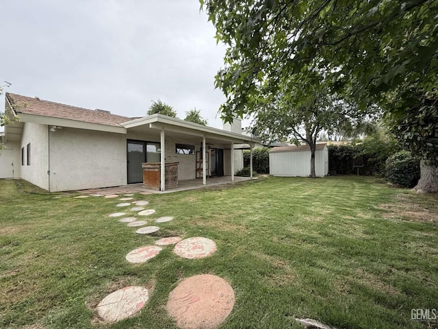 rear view of property with a lawn, an outbuilding, a storage unit, a patio, and stucco siding