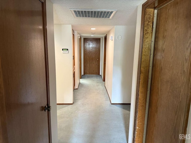 hallway with visible vents, a textured ceiling, and baseboards