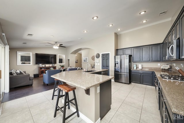 kitchen with arched walkways, light stone counters, stainless steel appliances, and light tile patterned floors