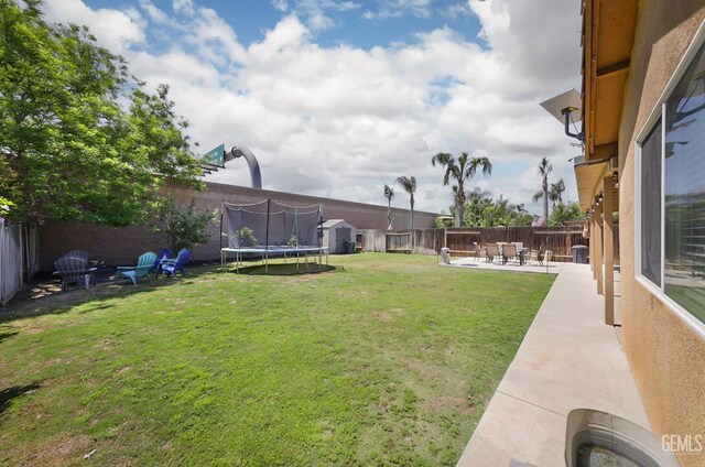 view of yard with a trampoline, a fenced backyard, and a patio