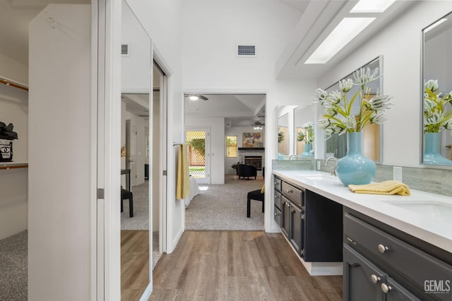 bathroom featuring a sink, double vanity, a ceiling fan, wood finished floors, and visible vents