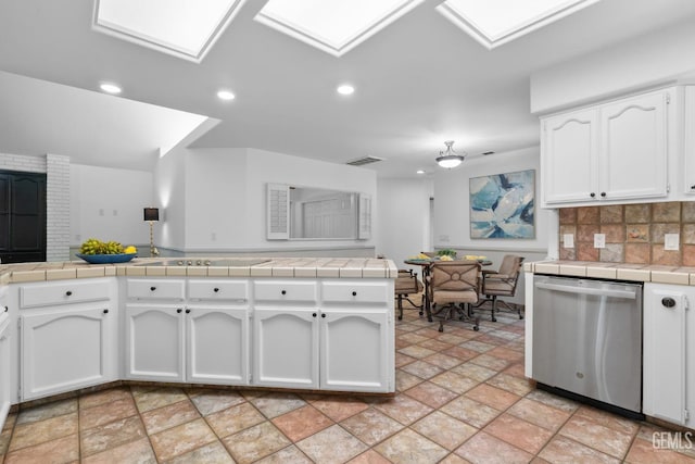 kitchen featuring tile counters, stainless steel dishwasher, stone finish flooring, and white cabinets