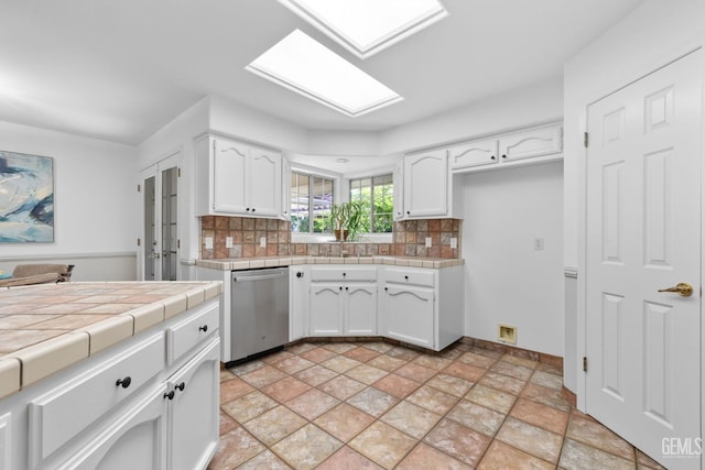 kitchen with stainless steel dishwasher, tile counters, white cabinets, tasteful backsplash, and a skylight