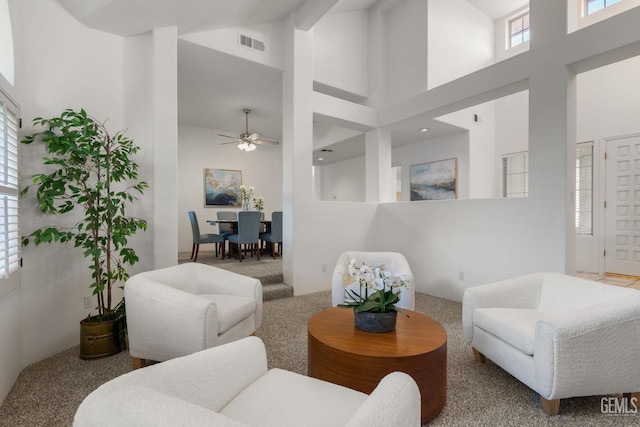 carpeted living area featuring visible vents, a ceiling fan, and a towering ceiling