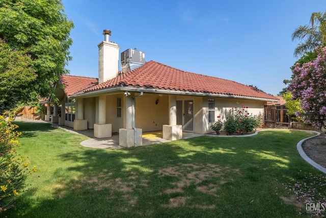 rear view of house with fence, a patio, a chimney, a tiled roof, and a yard