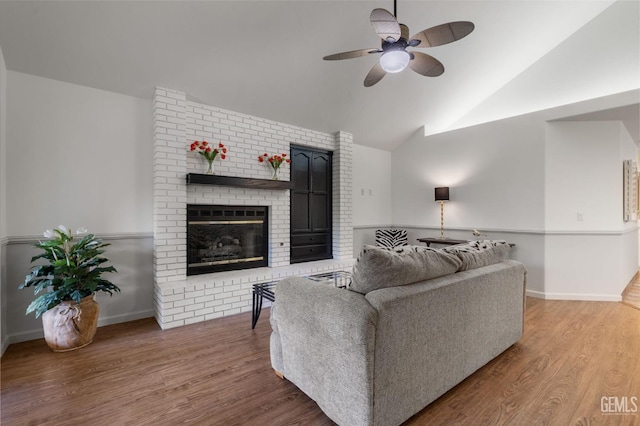living area with a brick fireplace, ceiling fan, wood finished floors, and vaulted ceiling