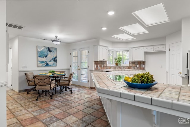 kitchen with white cabinets, tile counters, french doors, backsplash, and visible vents