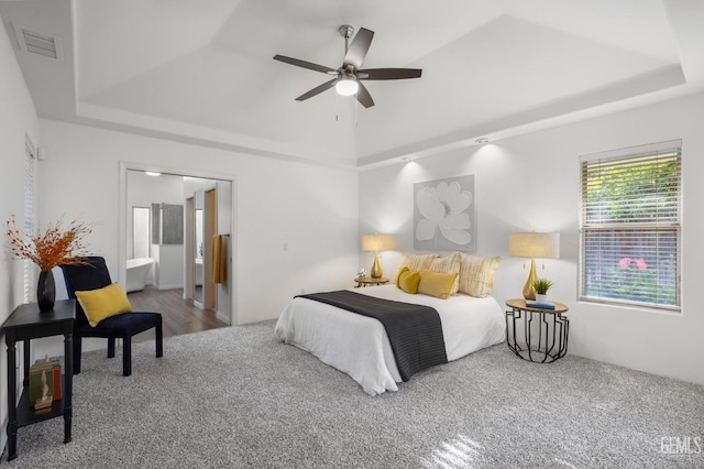 bedroom featuring a ceiling fan, visible vents, carpet floors, ensuite bathroom, and a tray ceiling