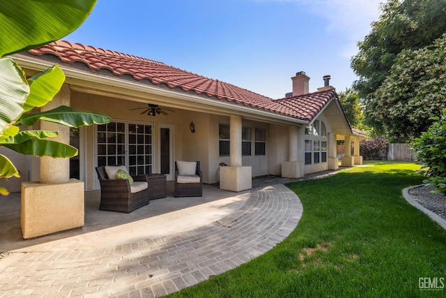 rear view of property with ceiling fan, a chimney, a patio area, a lawn, and a tiled roof