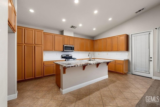 kitchen with a kitchen bar, appliances with stainless steel finishes, light stone countertops, a center island with sink, and lofted ceiling