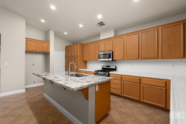 kitchen featuring sink, lofted ceiling, decorative backsplash, a center island with sink, and appliances with stainless steel finishes