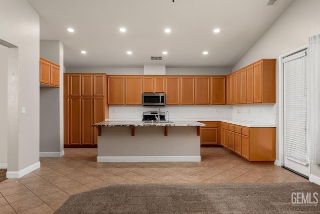 kitchen featuring vaulted ceiling, a kitchen bar, a kitchen island with sink, light tile patterned floors, and appliances with stainless steel finishes