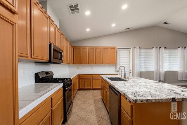 kitchen featuring dishwasher, sink, black gas stove, vaulted ceiling, and a kitchen island with sink