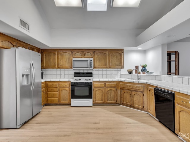 kitchen with decorative backsplash, appliances with stainless steel finishes, light wood-type flooring, sink, and tile counters