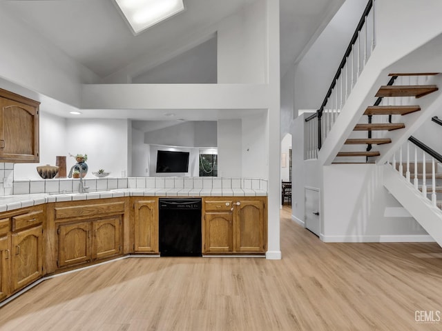 kitchen featuring tile counters, dishwasher, sink, and high vaulted ceiling