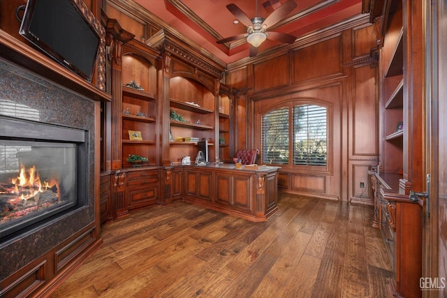 office with dark wood-type flooring, a premium fireplace, ceiling fan, ornamental molding, and built in shelves