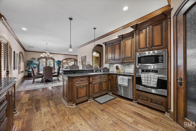 kitchen with sink, hardwood / wood-style flooring, appliances with stainless steel finishes, hanging light fixtures, and kitchen peninsula