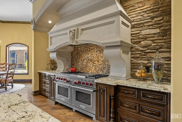 kitchen with dark brown cabinetry, crown molding, tasteful backsplash, light hardwood / wood-style floors, and range with two ovens