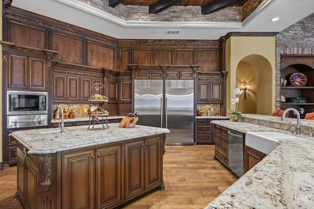 kitchen with light stone counters, built in appliances, sink, and decorative backsplash