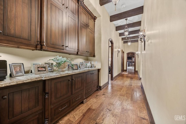 bar with beamed ceiling, decorative light fixtures, light stone counters, and light wood-type flooring