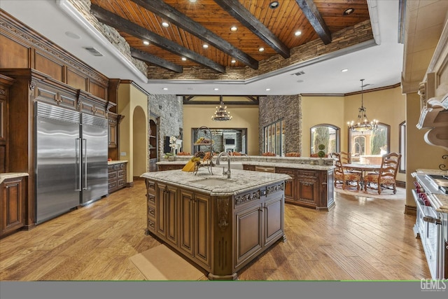 kitchen with beamed ceiling, an island with sink, a chandelier, premium appliances, and hanging light fixtures