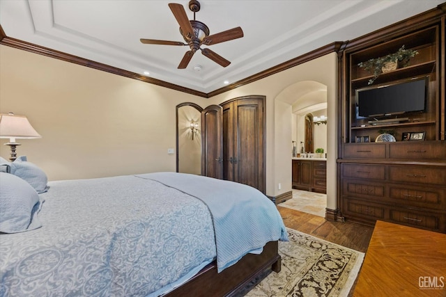 bedroom featuring ornamental molding, ceiling fan, ensuite bath, and light hardwood / wood-style flooring