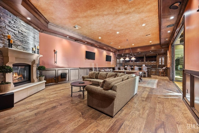 living room with ornamental molding, a tray ceiling, a fireplace, and light hardwood / wood-style floors