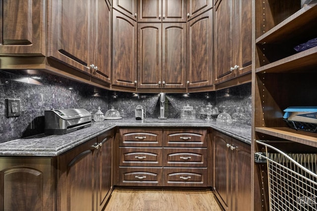 kitchen featuring dark brown cabinetry, tasteful backsplash, light hardwood / wood-style floors, and dark stone countertops