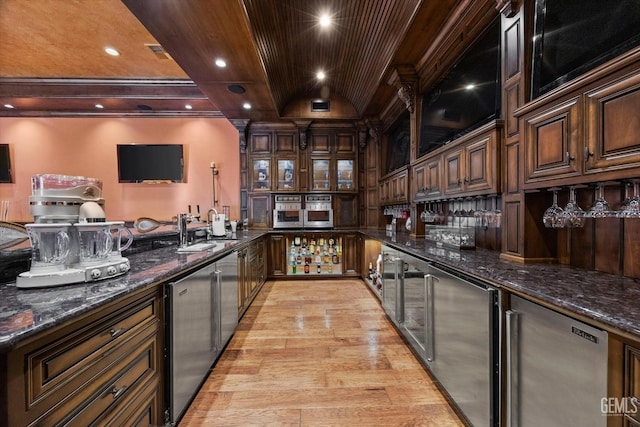 bar featuring sink, dark stone countertops, beverage cooler, dark brown cabinetry, and light hardwood / wood-style floors