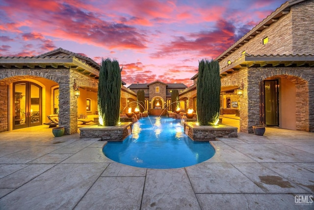 pool at dusk featuring a patio, a fireplace, and pool water feature