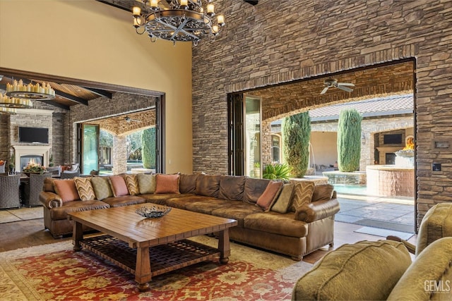 living room featuring an inviting chandelier, light hardwood / wood-style flooring, beamed ceiling, a towering ceiling, and exterior fireplace