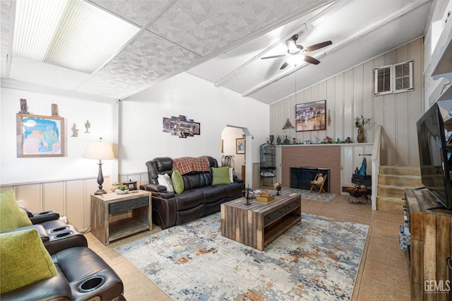 tiled living room with ceiling fan, wood walls, lofted ceiling, and a fireplace