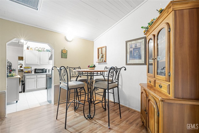 dining room featuring light wood-type flooring, crown molding, and vaulted ceiling