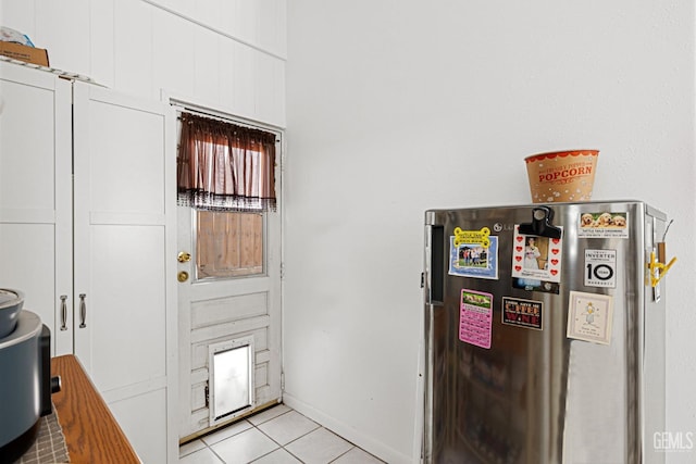 interior space with white cabinets, stainless steel fridge, and light tile patterned floors