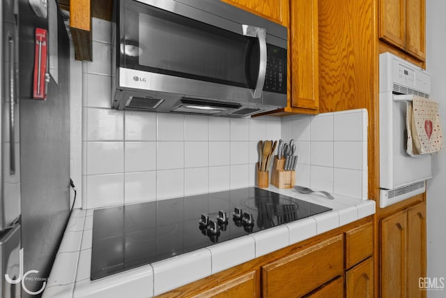 3713 Sechrest Ave, Bakersfield, CA 93309 - kitchen with stainless steel microwave, tile countertops, brown cabinetry, and tasteful backsplash