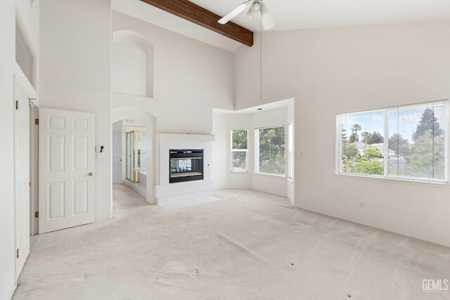 unfurnished living room with a multi sided fireplace, high vaulted ceiling, beamed ceiling, and light carpet