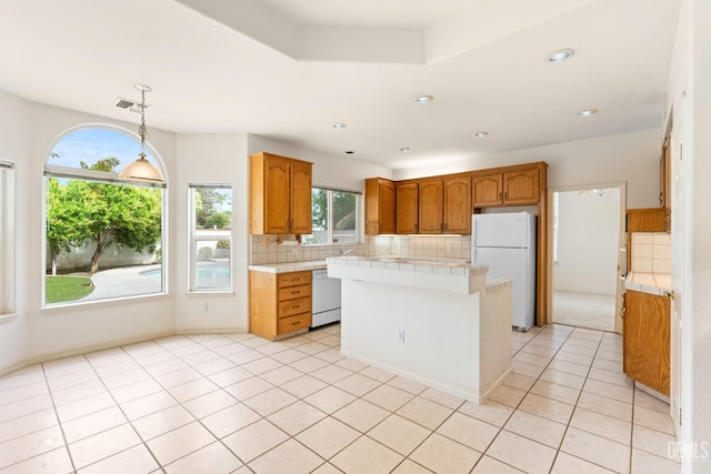 kitchen featuring light tile patterned floors, decorative backsplash, light countertops, a kitchen island, and white appliances