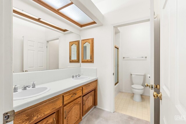 full bathroom with bath / shower combo with glass door, toilet, double vanity, and a sink