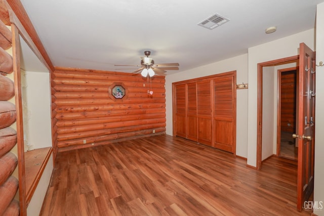 unfurnished bedroom featuring ceiling fan, a closet, log walls, and hardwood / wood-style flooring