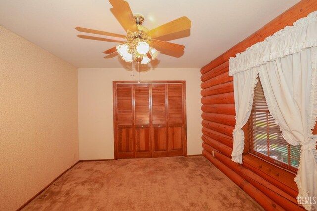 unfurnished bedroom with carpet flooring, ceiling fan, a closet, and log walls