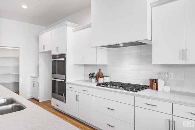 12914 Altair Ct, Bakersfield, CA 93314 - kitchen with white cabinetry, double wall oven, stainless steel gas cooktop, custom exhaust hood, and light wood finished floors