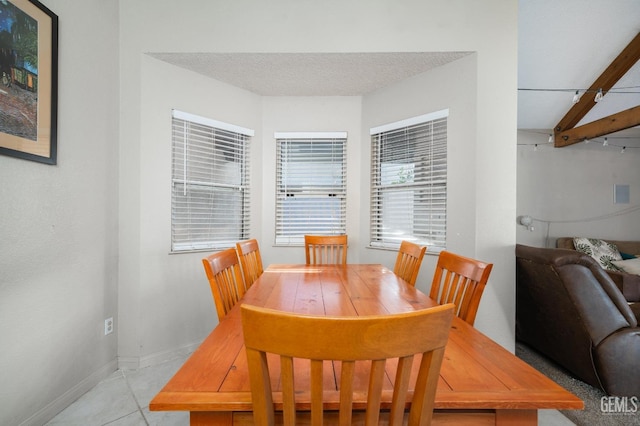 dining space with beam ceiling, light tile patterned floors, and a textured ceiling