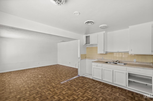 kitchen featuring dark parquet flooring, backsplash, a textured ceiling, sink, and white cabinetry