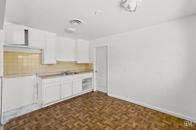 kitchen with dark parquet floors, backsplash, white cabinetry, and sink